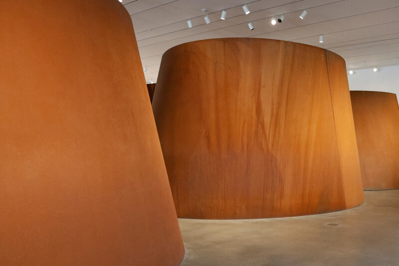 Large curved wooden sculptural forms in a minimalist gallery space with track lighting