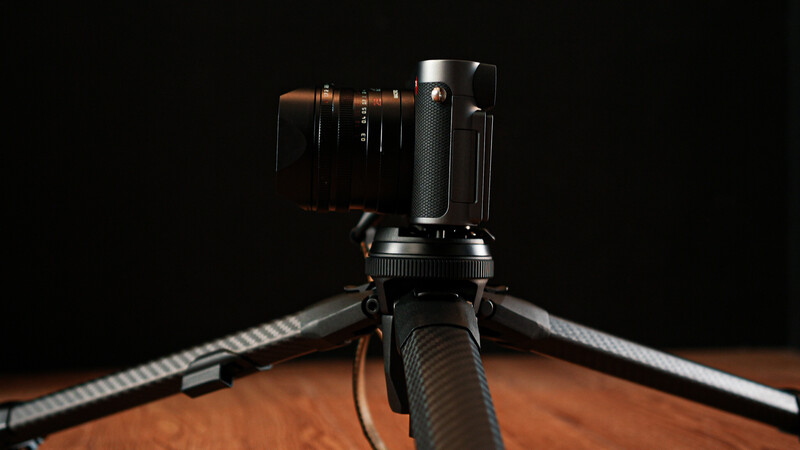Compact camera mounted on tripod with articulating arm against black background