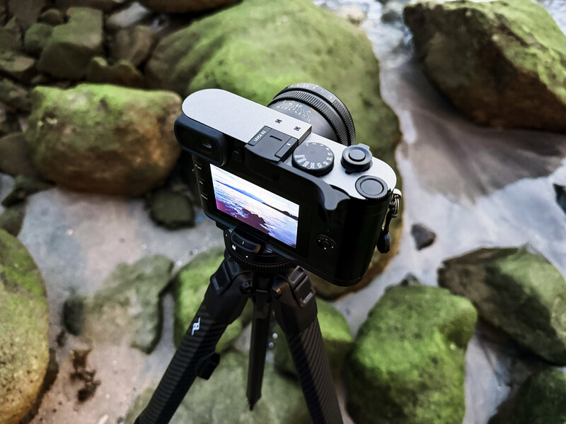 Mirrorless camera on tripod mounted over moss-covered rocks and stream