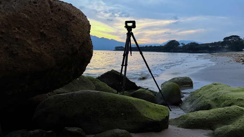 Camera on tripod positioned on moss-covered rocks at a beach during golden hour sunset