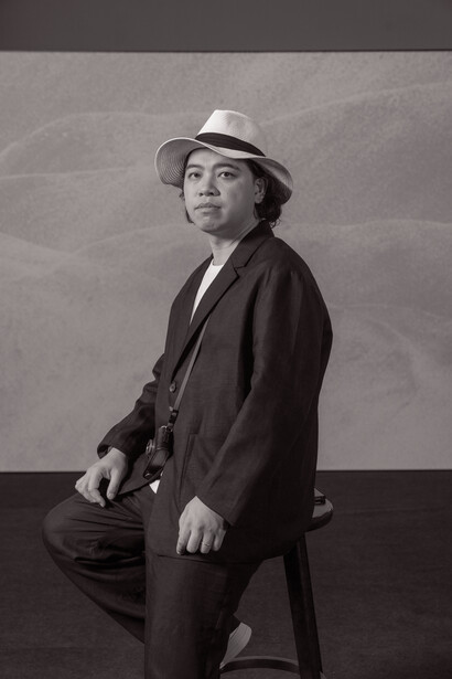 Man in dark suit and fedora hat posed against neutral gray background