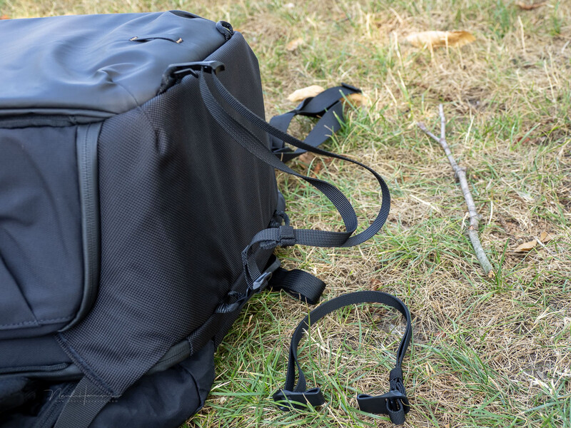 Black camera backpack with curved carabiners attached to side handles on grass