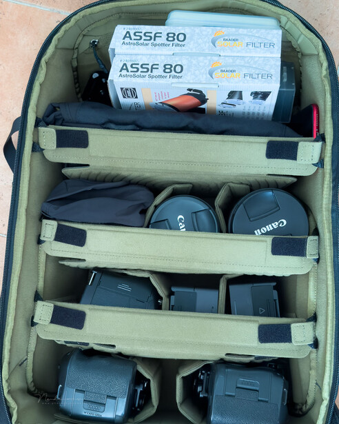 Open camera backpack with organized gear compartments showing lenses, batteries, and accessories