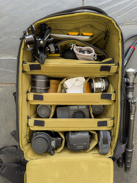 Yellow camera backpack organizer displaying lenses, camera bodies, and photography accessories across four compartments