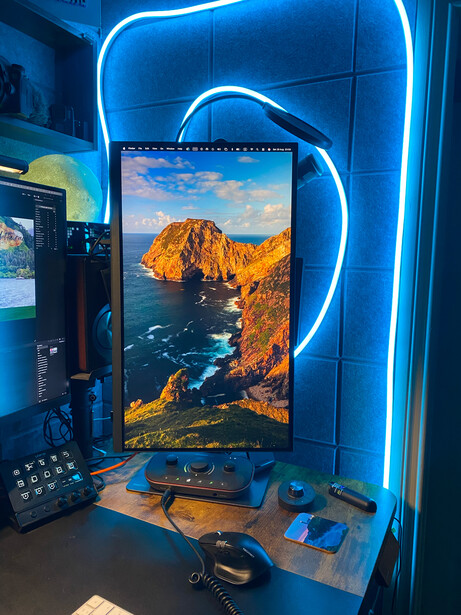 Monitor displaying landscape photograph framed by blue neon lighting in studio setup