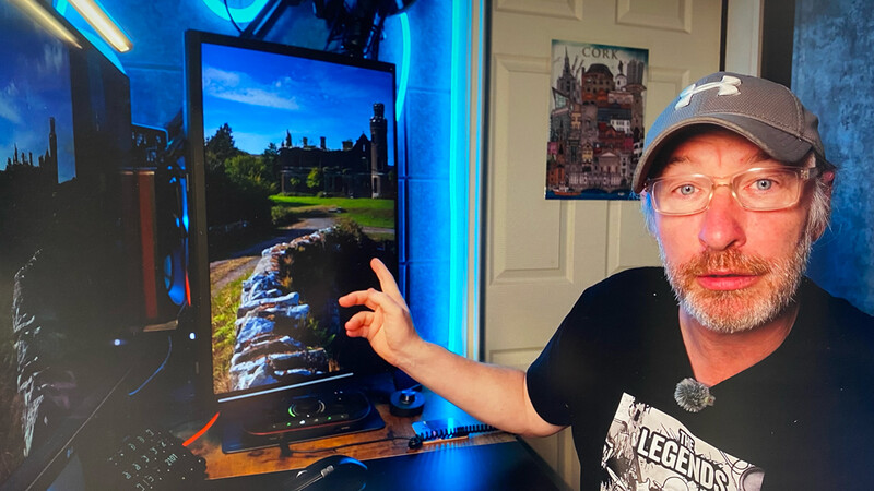 Man pointing at computer monitor displaying landscape photography with blue accent lighting