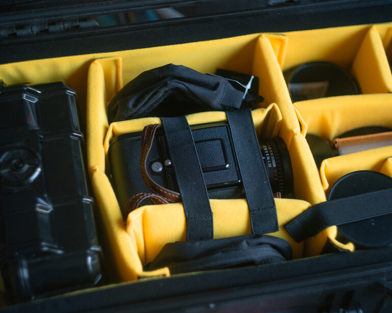Camera gear organized in yellow foam-lined storage compartments with black straps