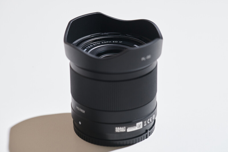 Black wide-angle camera lens with petal lens hood on neutral background