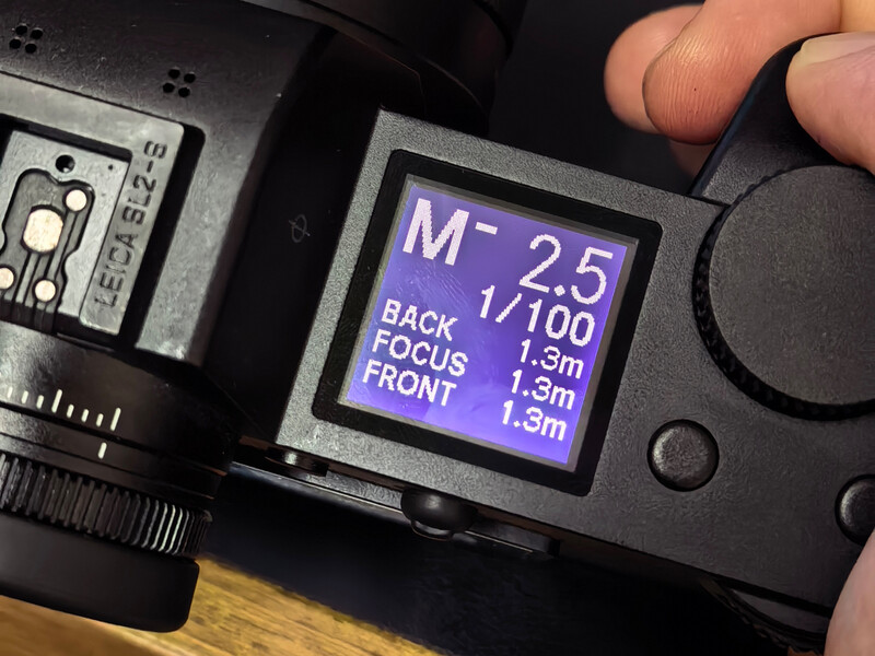 Camera LCD screen displaying manual focus settings showing M-2.5, 1/100 shutter speed, and focus distance measurements