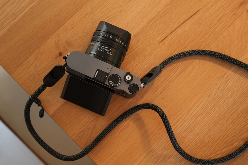 Rangefinder camera with attached lens and black camera strap on wooden surface