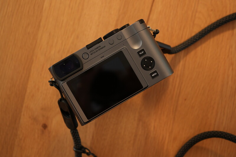 Compact rangefinder camera with rear LCD screen on wooden surface with shoulder strap