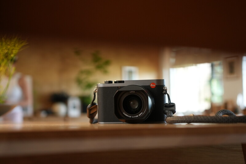 Black rangefinder camera with leather strap on wooden surface with blurred interior background