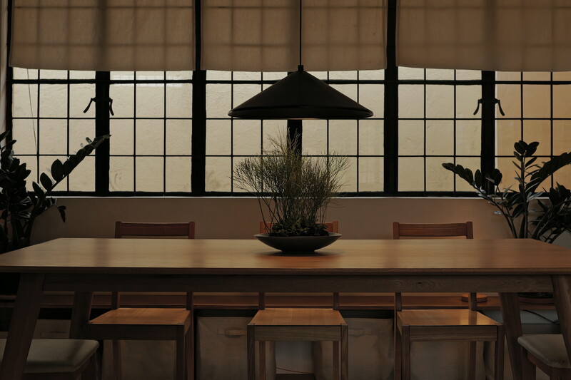 Minimalist dining space with pendant lamp, wooden table, and industrial grid windows