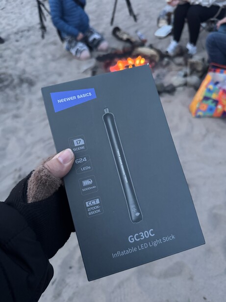 Hand holding Neewer GC-20C LED light kit box at beach bonfire gathering
