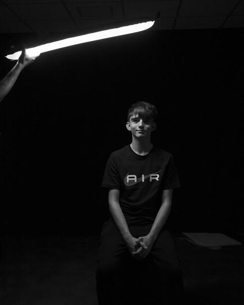 Person in dark clothing standing against black background under geometric linear studio light