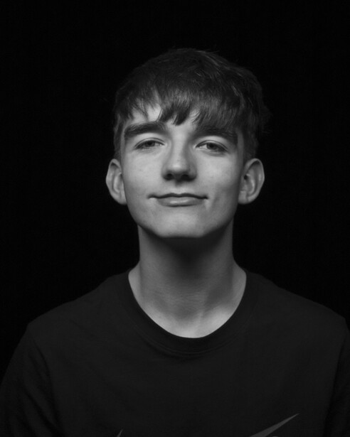 Black and white portrait of a young man with dark hair and bangs against a dark background