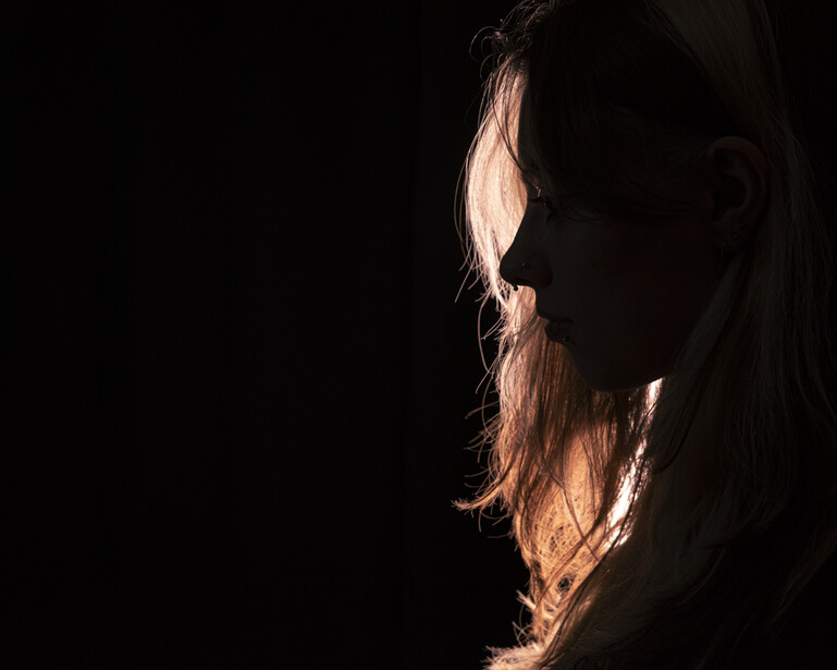 Side profile of a person with long hair backlit by warm golden light against black background