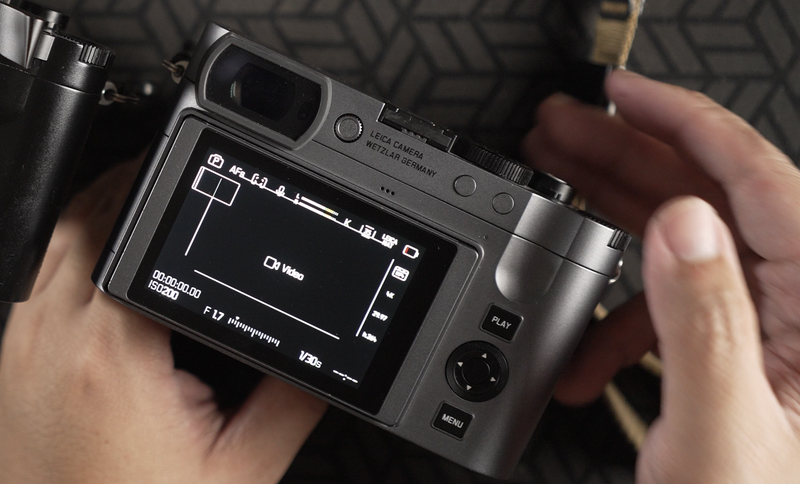 Hands holding a compact mirrorless camera with LCD screen displaying exposure settings and histogram