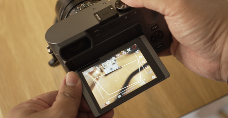 Hands holding mirrorless camera with articulating LCD screen displaying live view composition