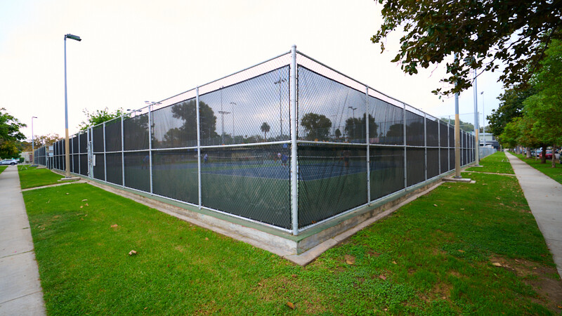 Modern tennis court with dark mesh enclosure and metal frame in park setting