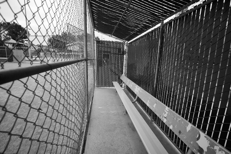 Black and white photograph of a narrow corridor with chain-link and vertical metal fencing