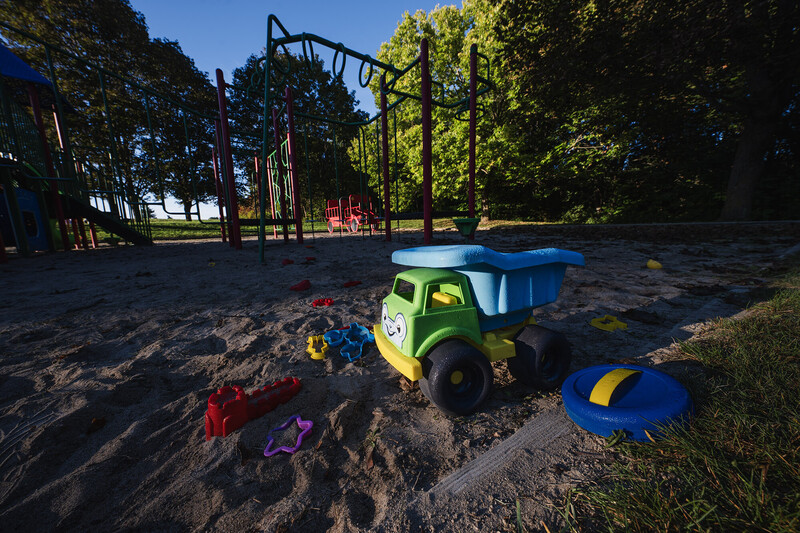 Colorful toy dump truck in sandbox with playground structures and trees in background