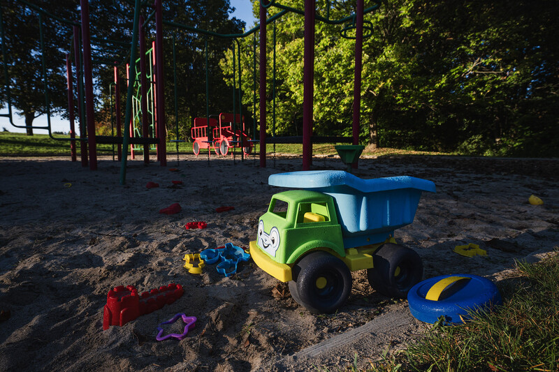 Green and blue toy dump truck in sandbox with playground equipment and trees in background
