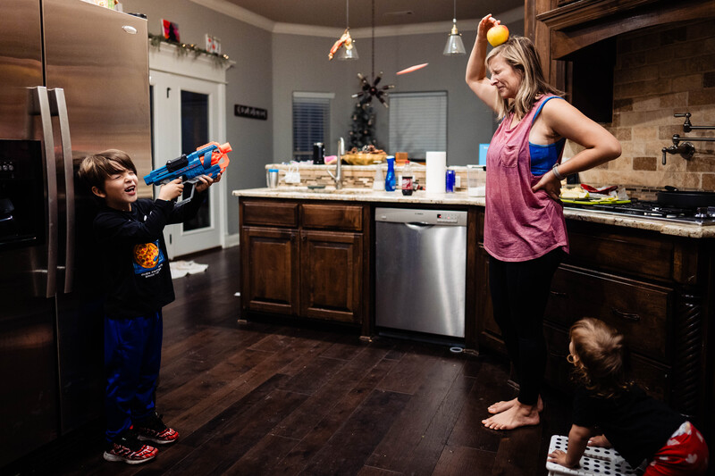 Woman in kitchen playing with children using toy foam dart blaster