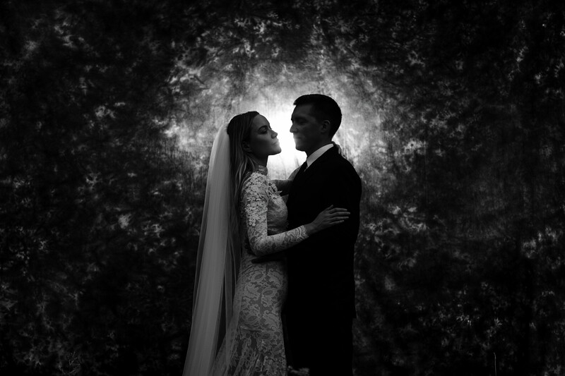 Bride and groom in formal embrace against textured dark background in black and white