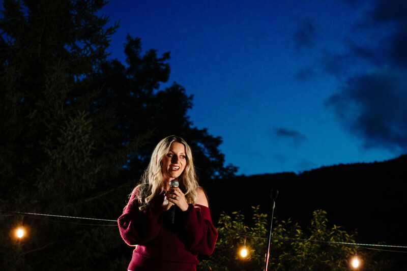 Woman in burgundy top wearing sunglasses against twilight sky with ambient lighting