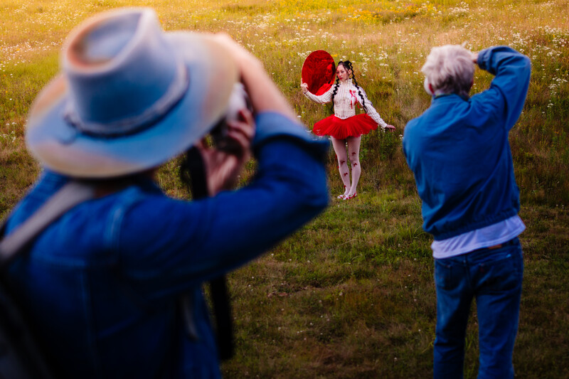 Two photographers in blue jackets shooting a child in a red dress in an open field