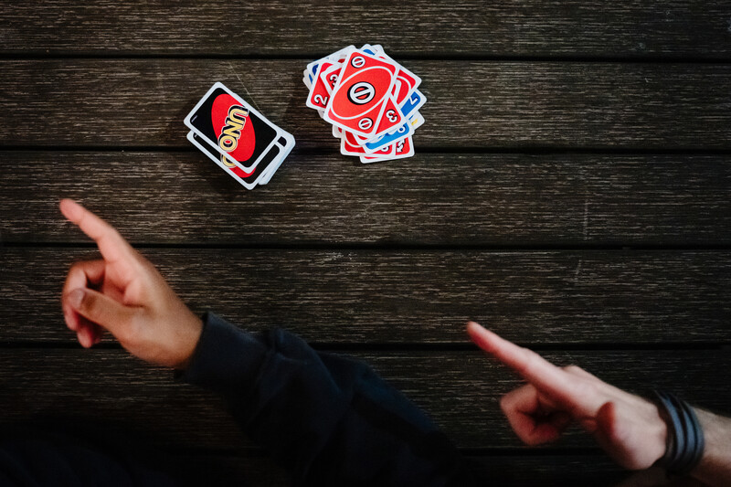Two hands pointing at red playing cards spread on dark wooden surface