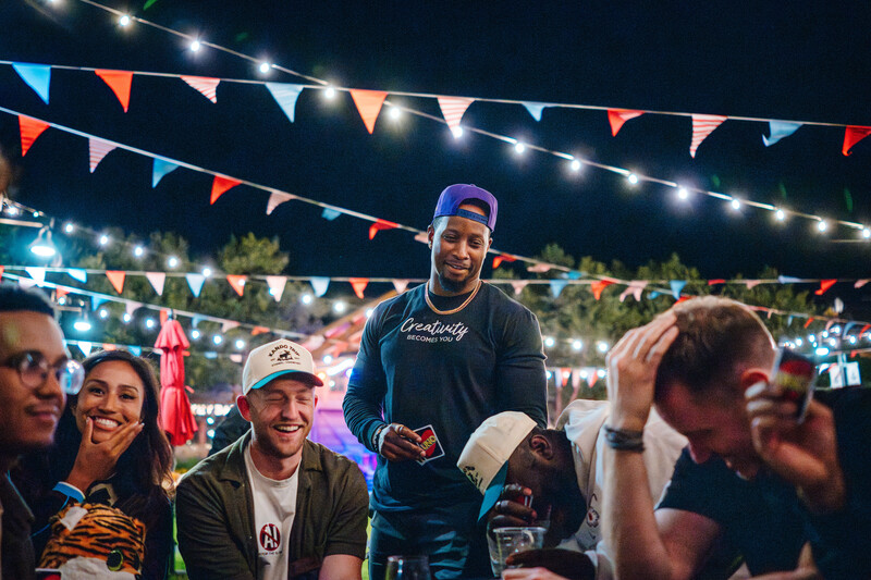 Group of people enjoying an outdoor nighttime event under string lights and bunting decorations
