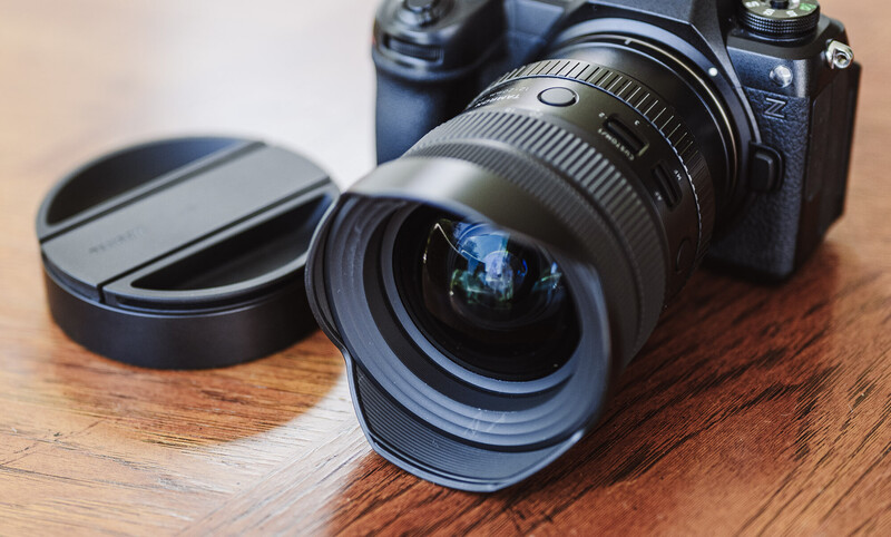 Wide-angle lens with lens cap on wooden surface next to mirrorless camera body