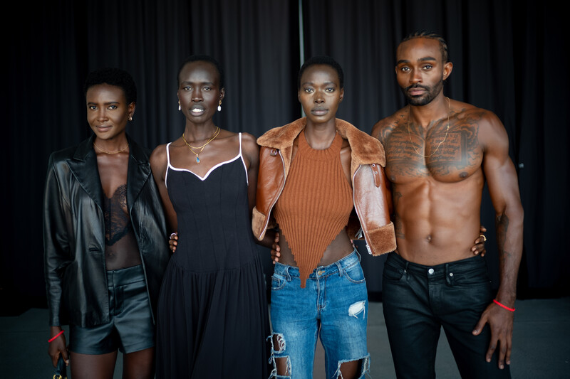 Four people in stylish casual and semi-formal wear posing against a dark curtain backdrop