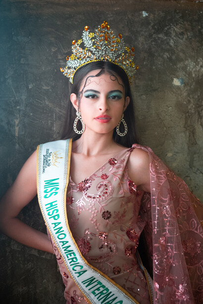 Woman wearing ornate golden tiara and formal beaded gown with pageant sash