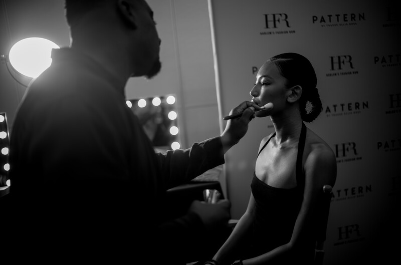 Makeup artist applying cosmetics to woman's face in front of lit vanity mirror