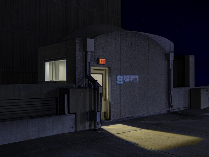 Cylindrical building with dark exterior illuminated at night, glowing doorway and exit sign visible