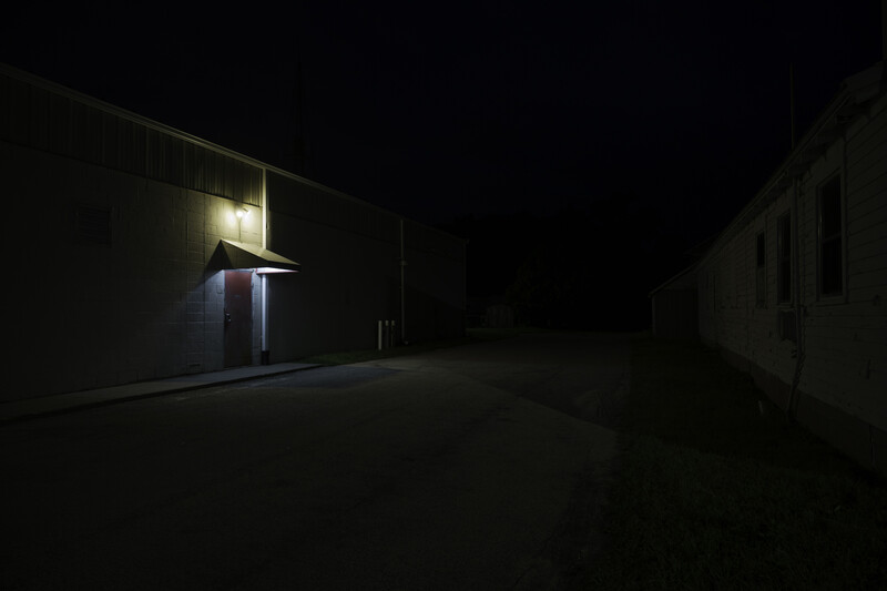 Minimalist nighttime composition of an illuminated building entrance on left with dark structures on right