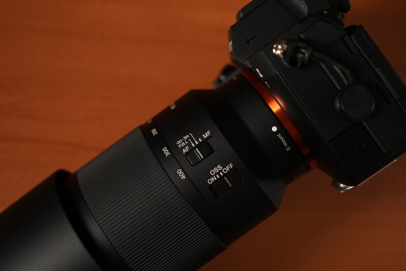 Telephoto lens mounted on mirrorless camera body against warm orange background