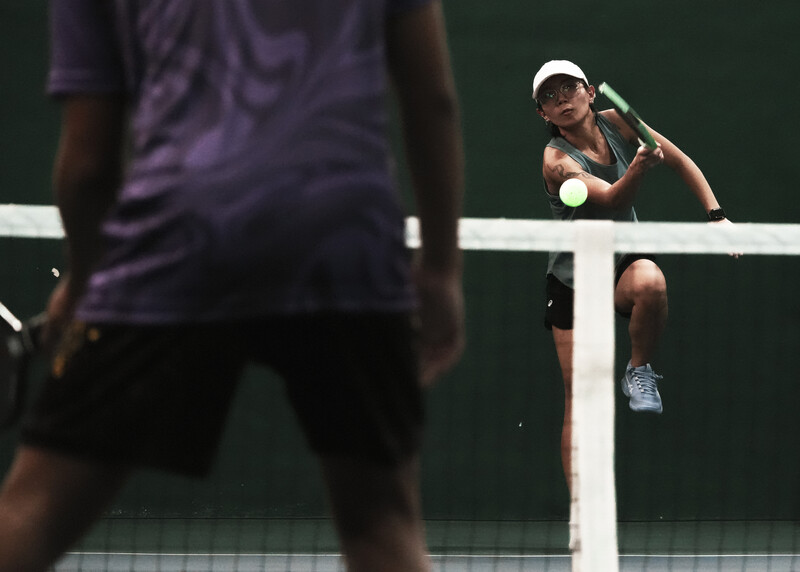 Tennis player in white cap executing a forehand volley at the net during match play