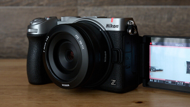 Nikon Z mirrorless camera with mounted lens next to external monitor on wooden surface