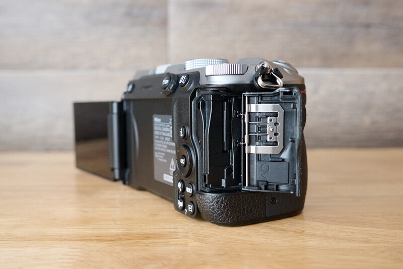 Black camera with open back panel showing internal mechanics and battery compartment on wooden surface