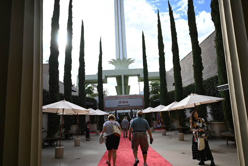 Red carpet event venue with cypress trees, white umbrellas, and illuminated cross in background