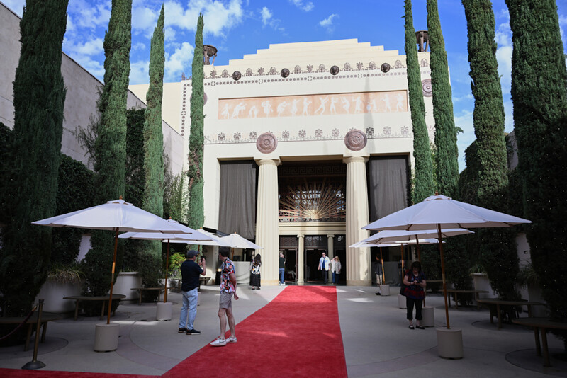 Art Deco building entrance with red carpet, white umbrellas, and cypress trees framing symmetrical facade