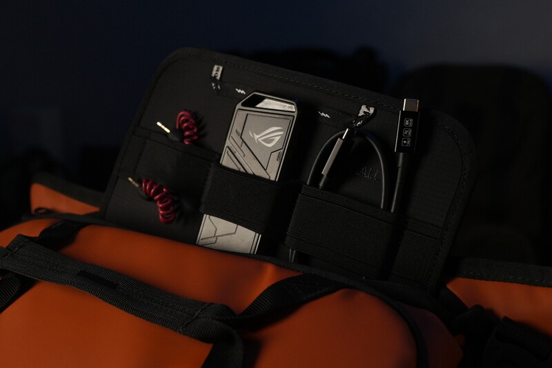 Black tech organizer pouch with compartments displayed on orange and black fabric