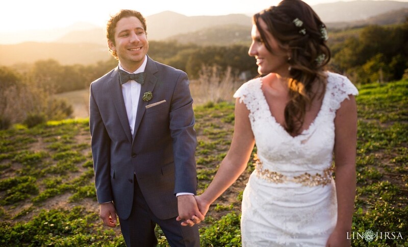 Bride and groom holding hands in a vineyard at golden hour with mountains in the background