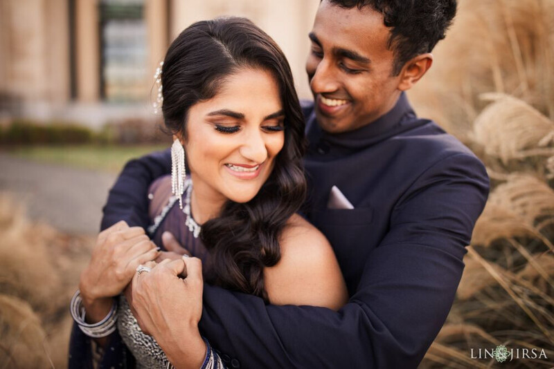 Man embracing woman from behind, both smiling at camera in outdoor setting