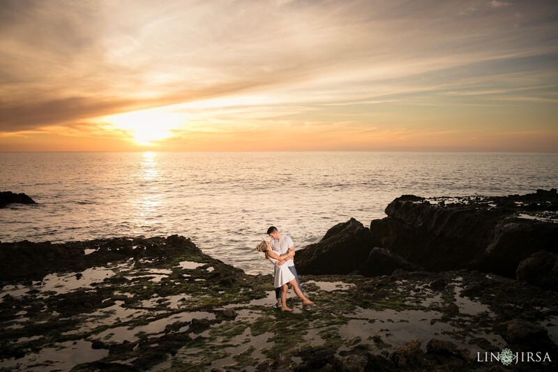 Couple embracing on rocky beach at sunset with golden ocean light