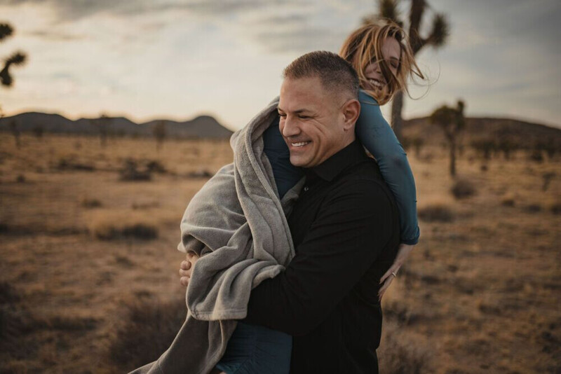 Man carrying woman on his shoulders in desert landscape at golden hour